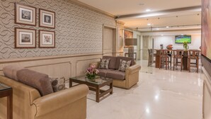 A spacious living room with a beige sofa set, a glass coffee table, and a patterned wallpaper.