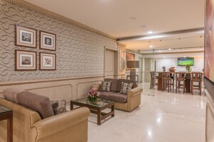 A spacious living room with a beige sofa set, a glass coffee table, and a patterned wallpaper.