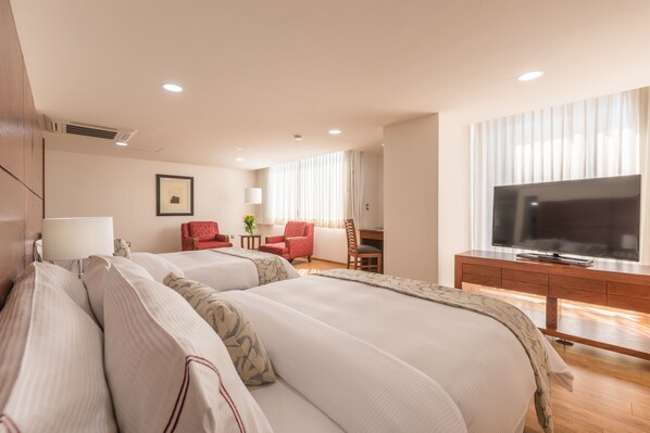 A hotel room with two beds, a desk, a TV, and a chair.