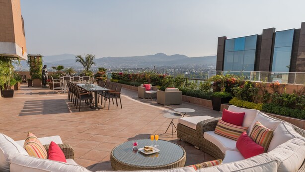 A rooftop patio with wicker furniture, a round table, and a view of the city and mountains.