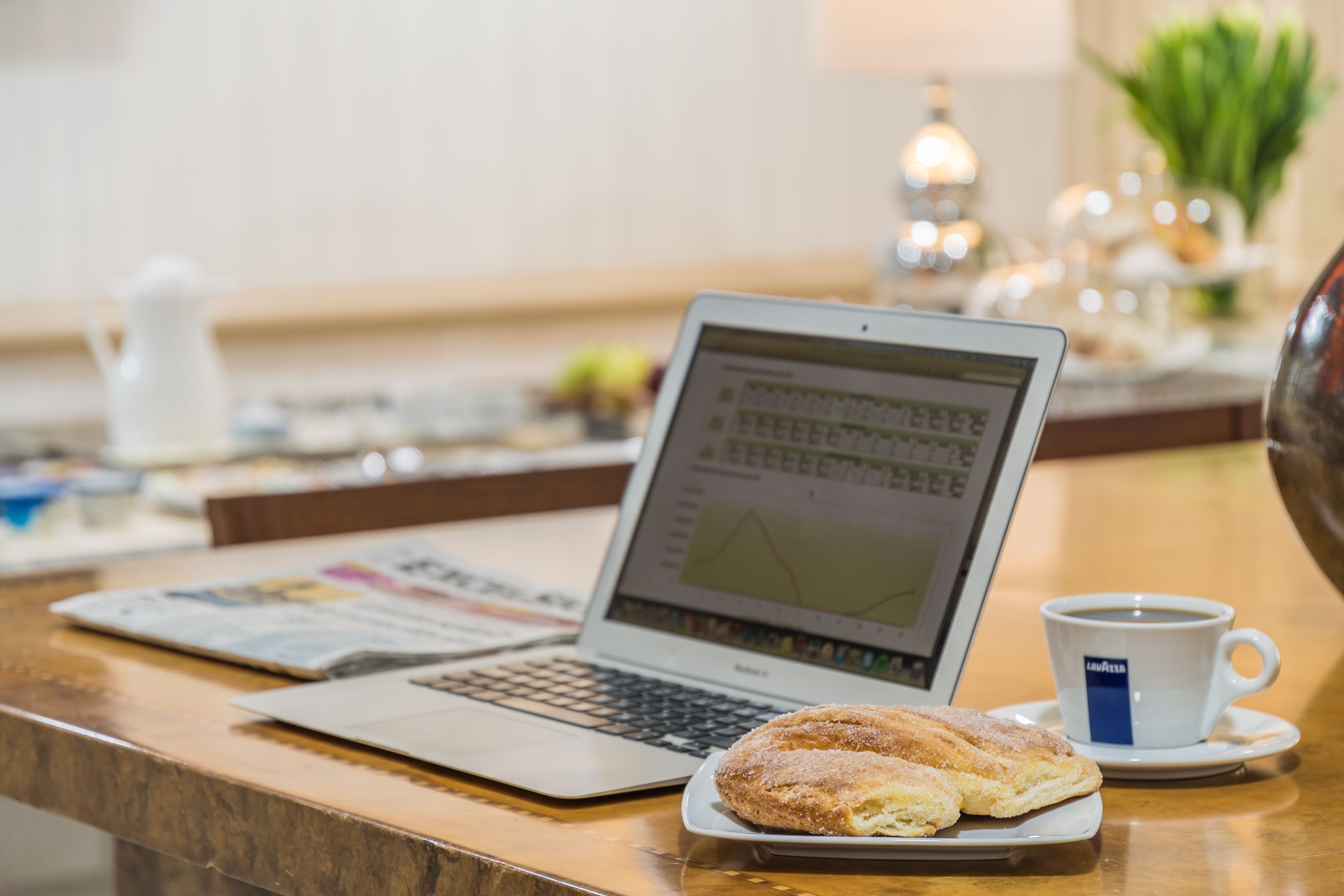 A laptop on a wooden table with a plate of pastries and a cup of coffee.