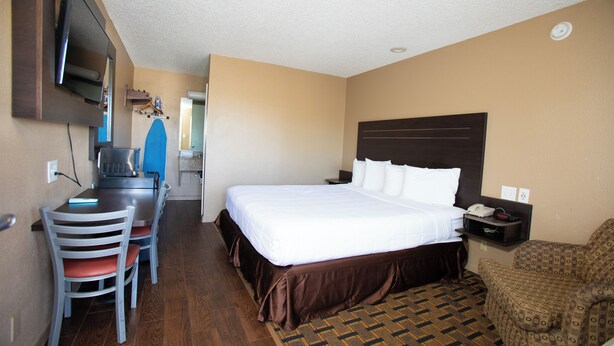 A hotel room with a bed, a desk with a chair, a television, and a patterned rug.