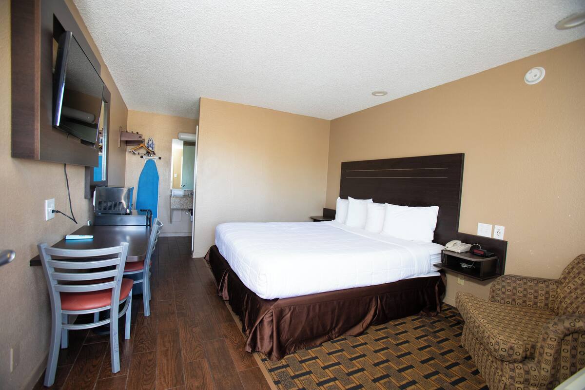 A hotel room with a bed, a desk with a chair, a television, and a patterned rug.