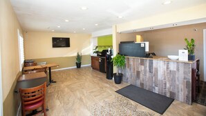 A modern hotel lobby with a reception desk, seating area, and a kitchen in the background.