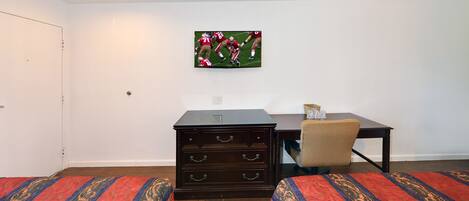 A hotel room with two beds, a dresser, a desk, and a television mounted on the wall.
