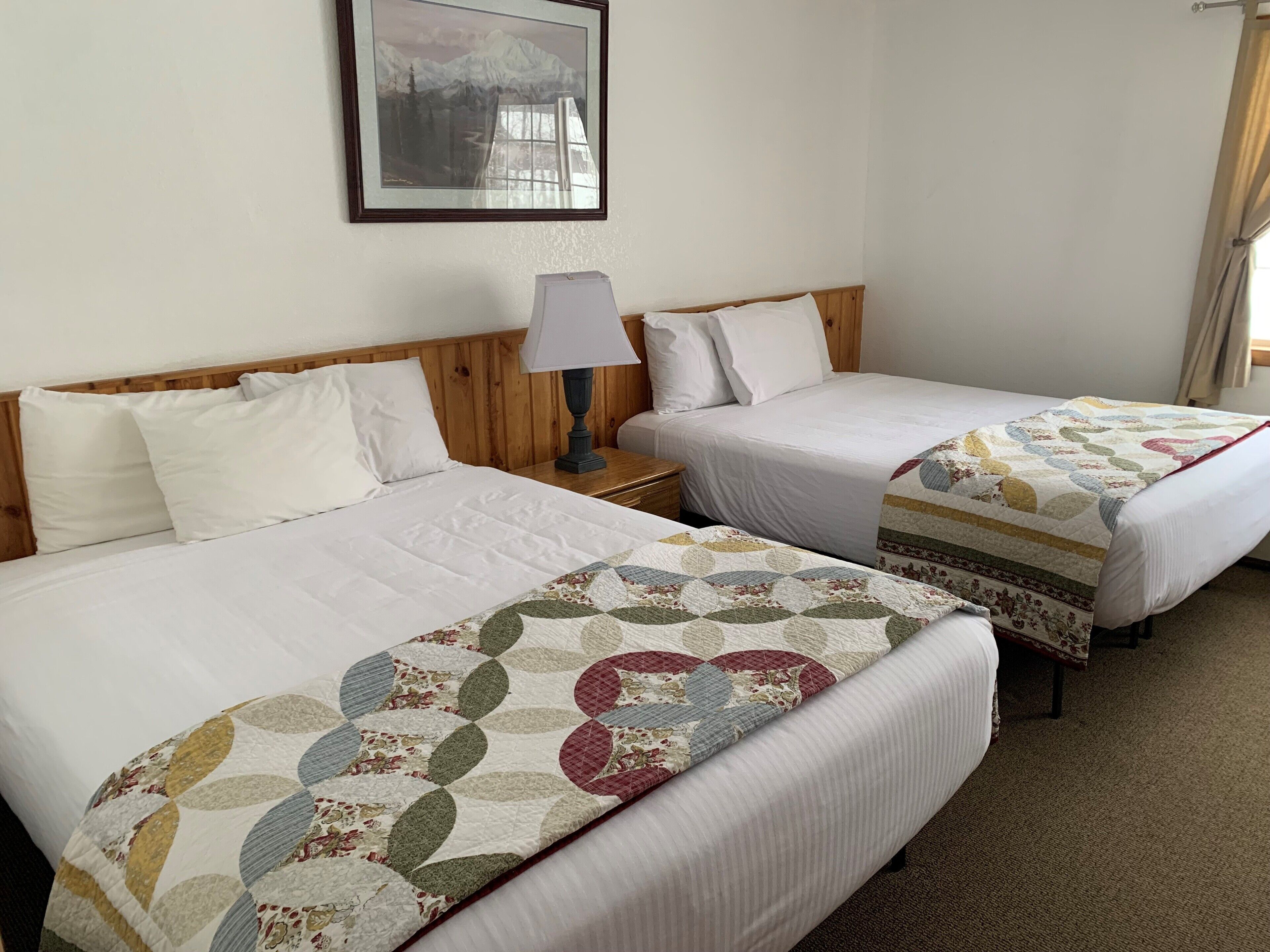 Two single beds with white linens, a wooden headboard, and a bedside table with a lamp.