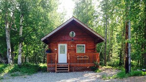 A wooden cabin with a front porch, a door, and a small window.