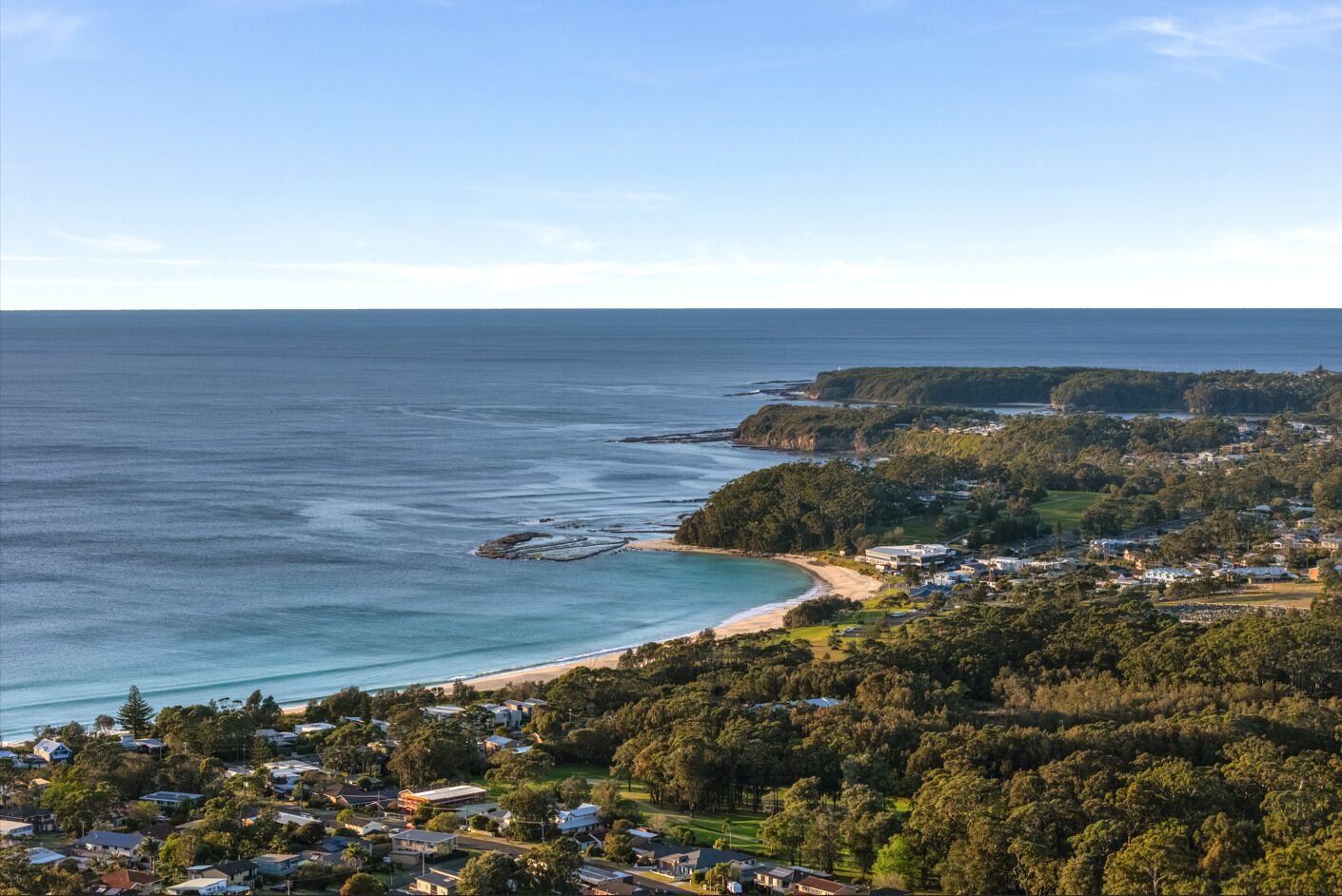 A coastal town with a beach, dense greenery, and residential buildings.
