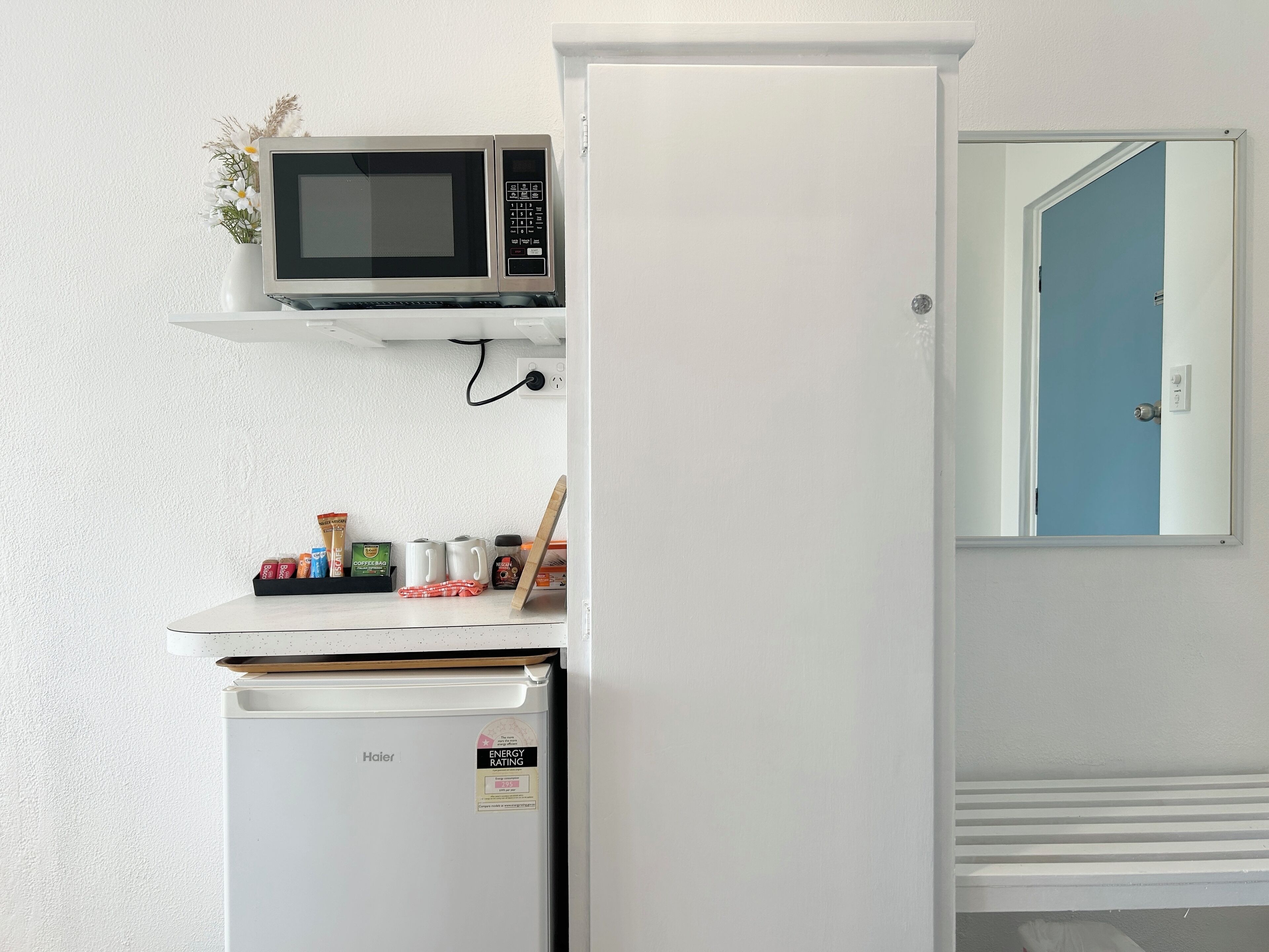 Une petite cuisine équipée d’un four à micro-ondes, d’un réfrigérateur et d’une petite étagère contenant divers objets.