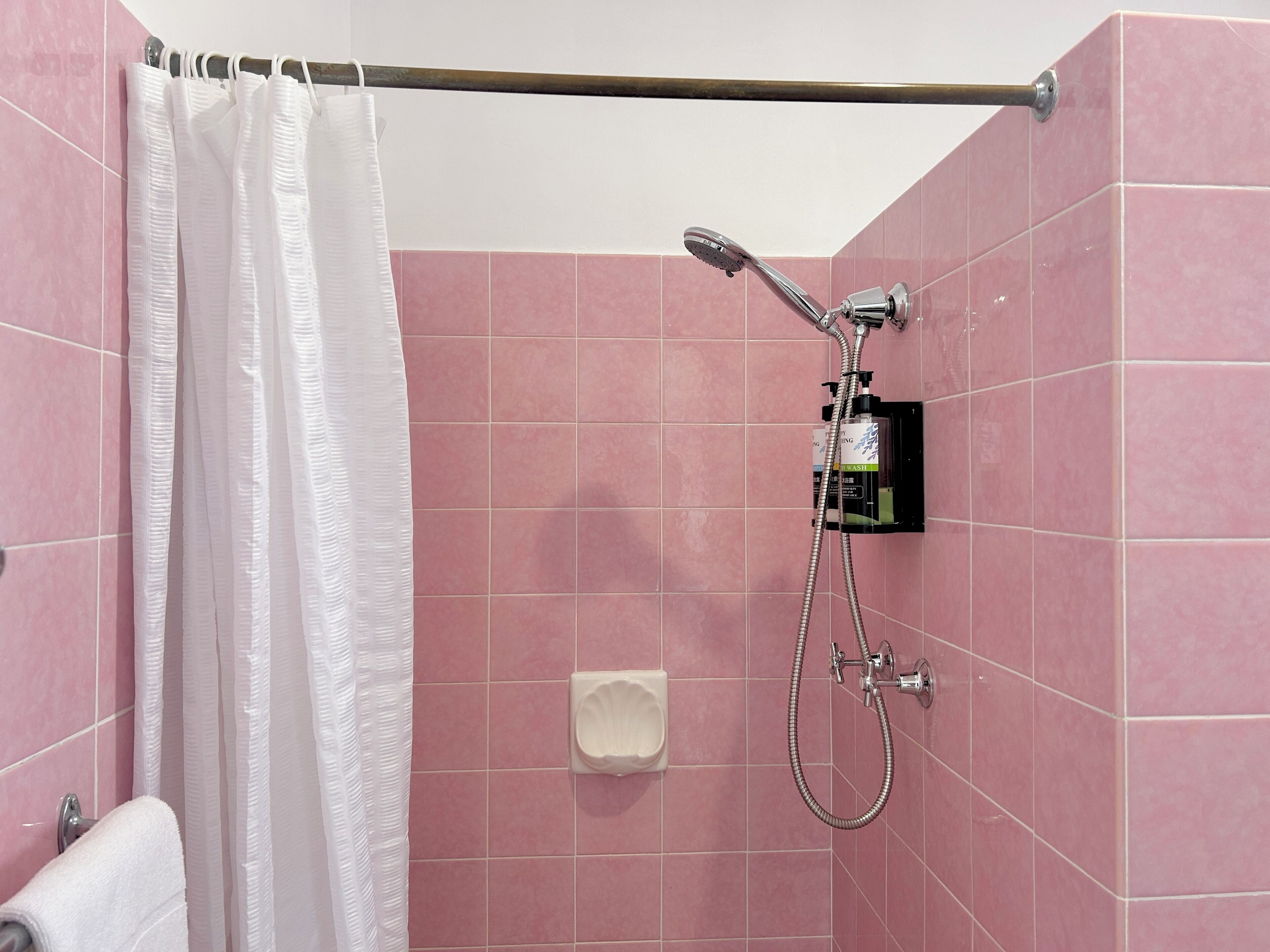 A shower with pink tiles, a white curtain, and a handheld showerhead.