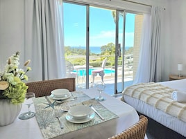 Habitación de hotel con balcón, una mesa de comedor para dos personas y una cama con vista al océano.