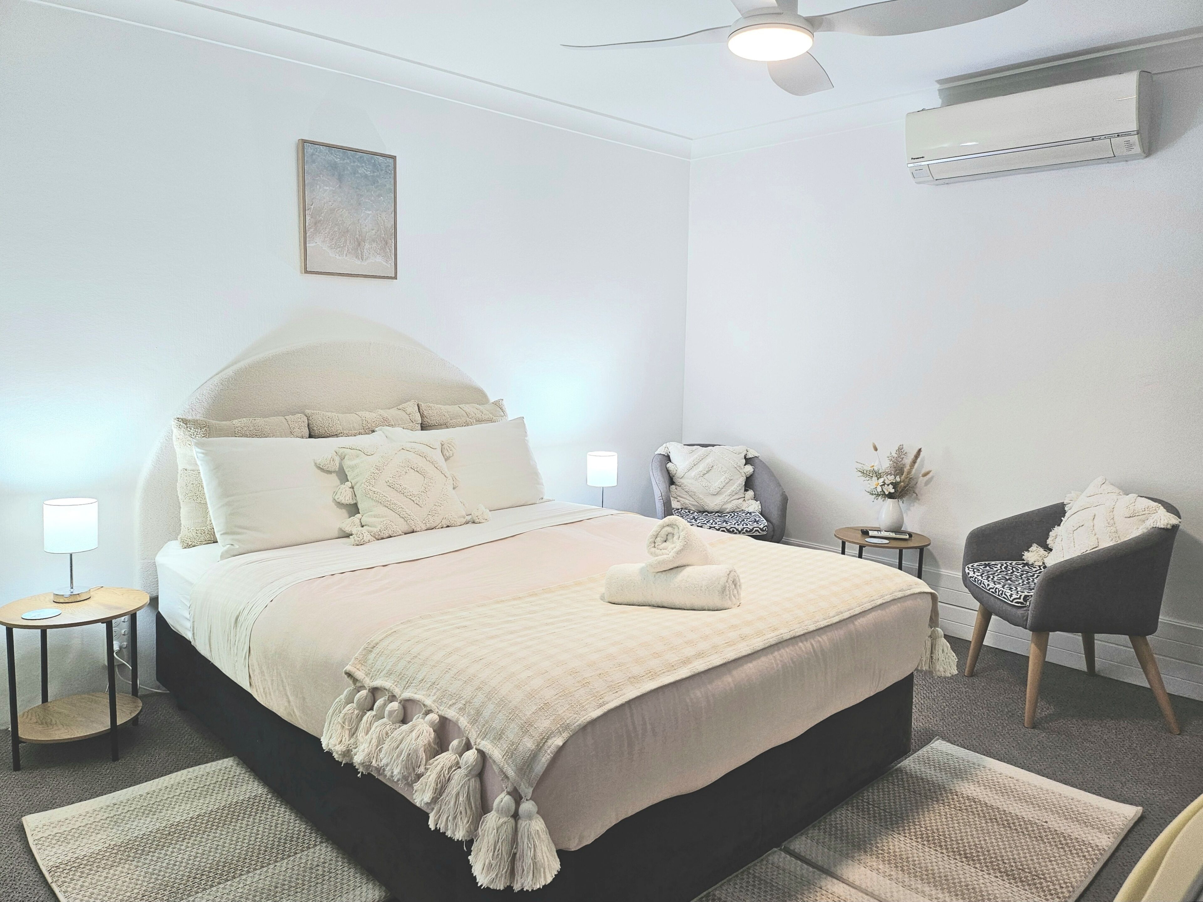 Een slaapkamer met een groot bed, een stoel, een klein tafeltje en een airconditioning.