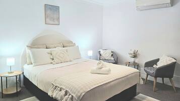 Une chambre à coucher avec un grand lit, une chaise, une petite table et un appareil de climatisation.