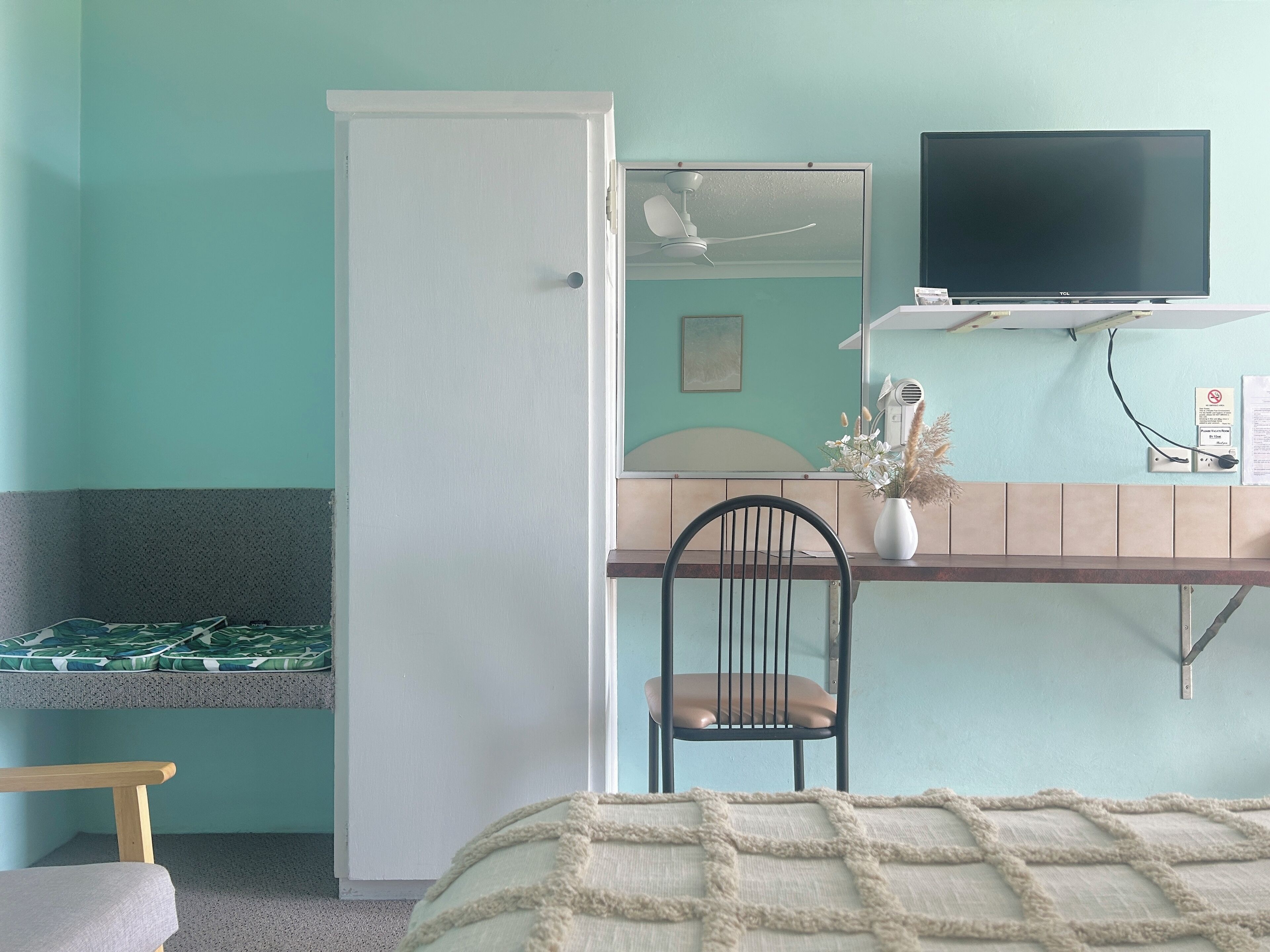 A room with a bed, a desk with a chair, a television, and a door.