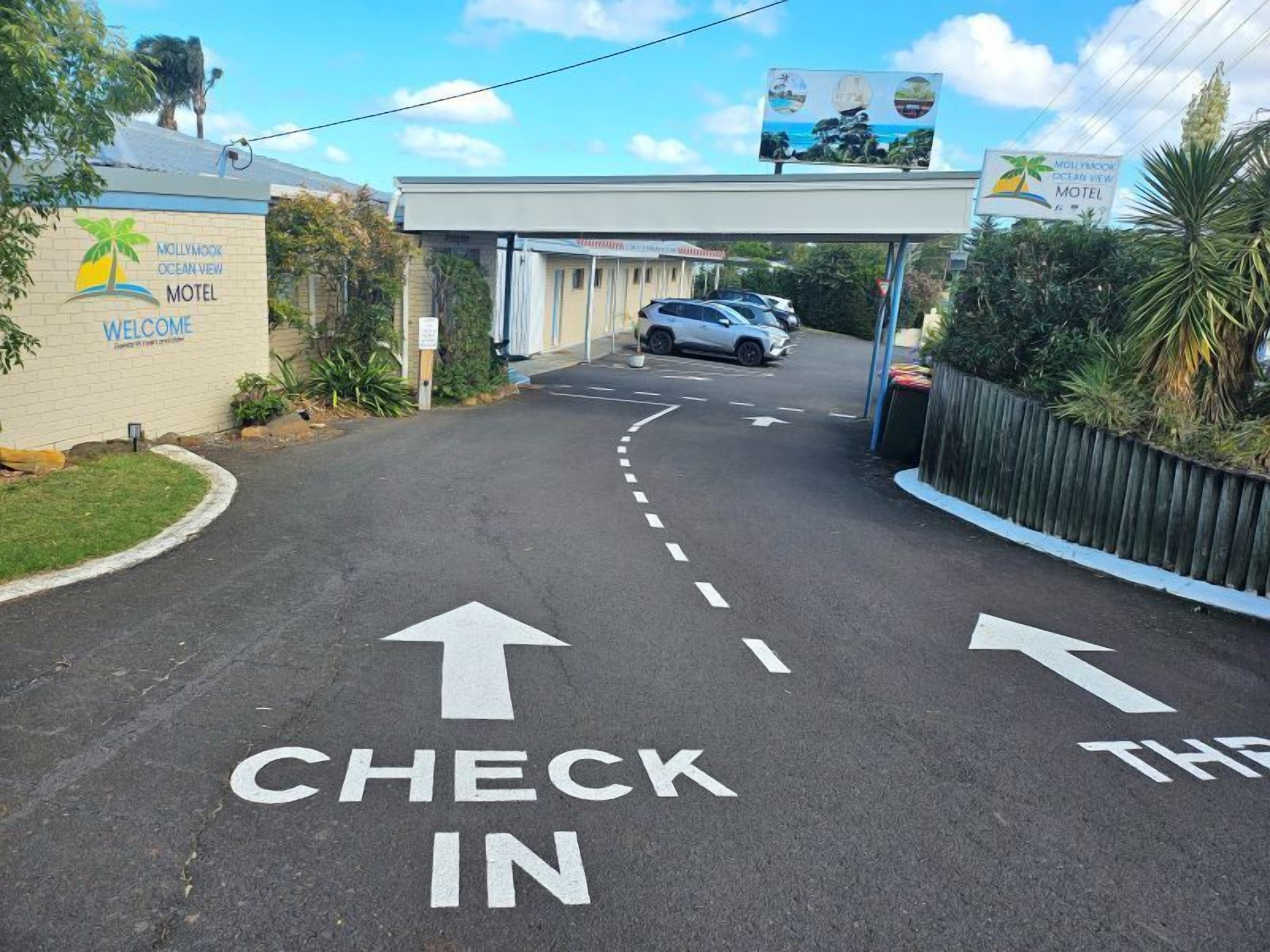 Entrada a un motel con un cartel que dice 'CHECK IN' y flechas direccionales en el pavimento.