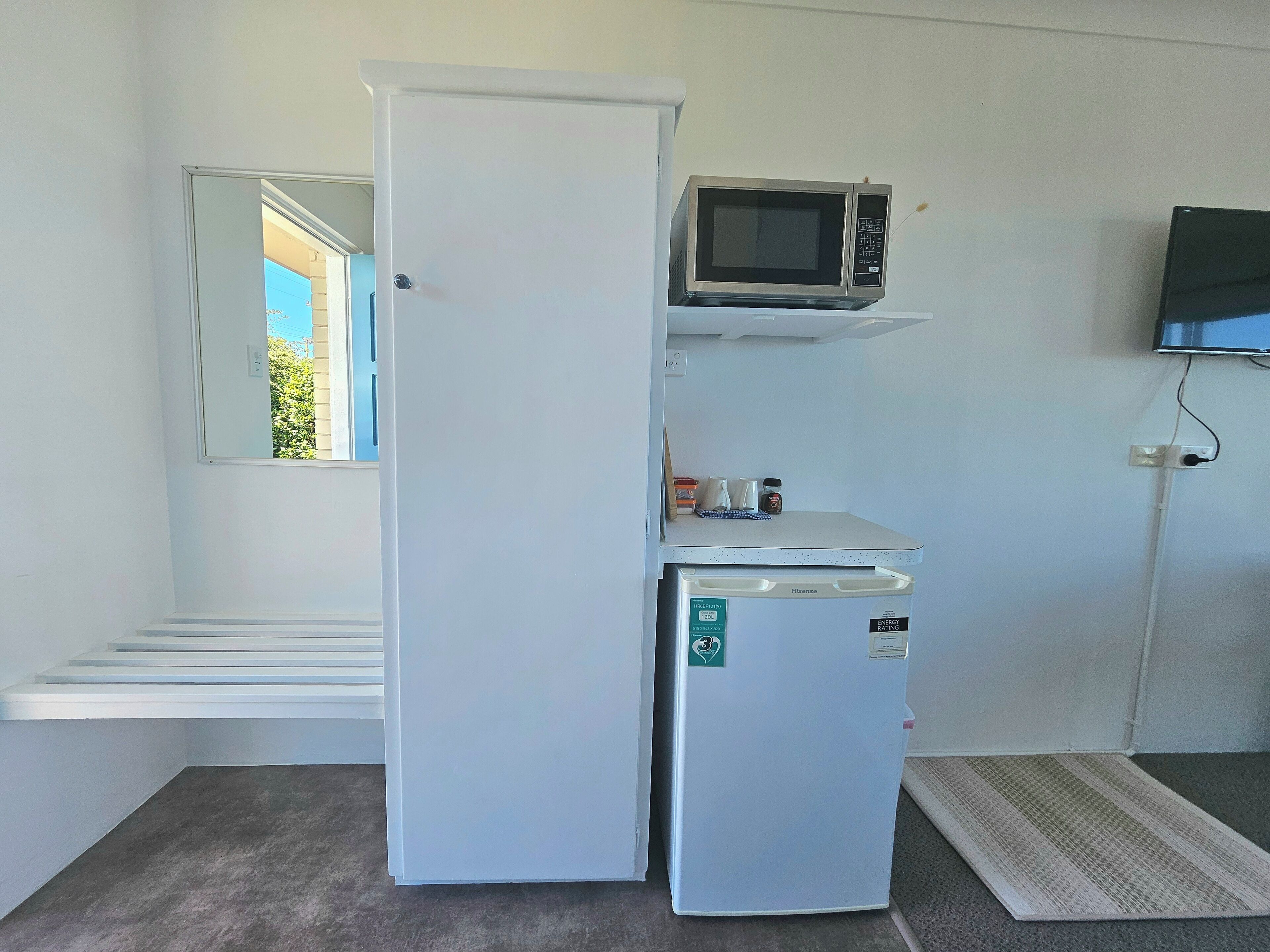 A compact kitchenette with a white refrigerator, a microwave, and a small countertop.