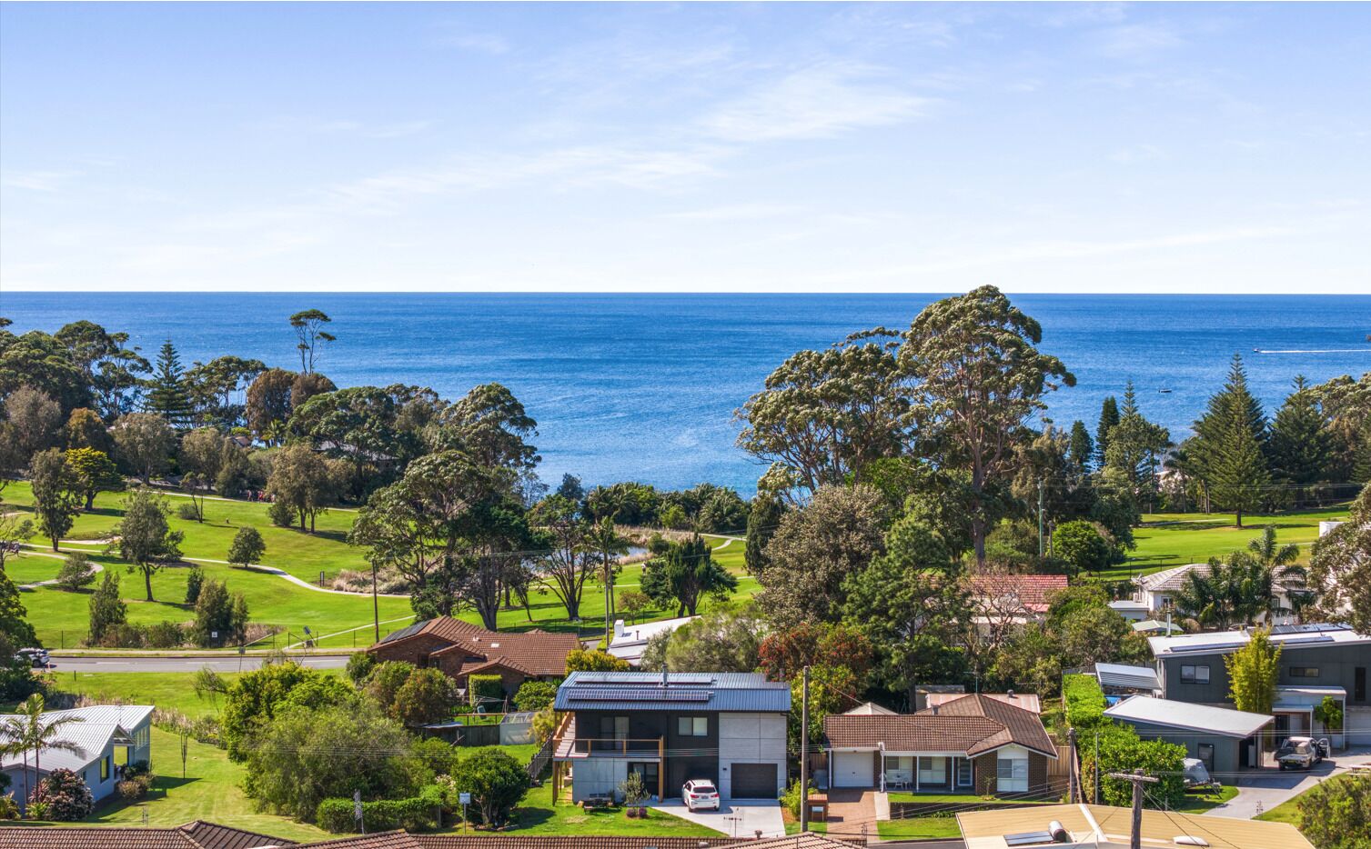 A coastal residential area with houses, a golf course, and a view of the ocean.