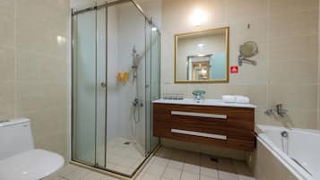 Un baño moderno con ducha de vidrio, tocador de madera, inodoro blanco y bañera.