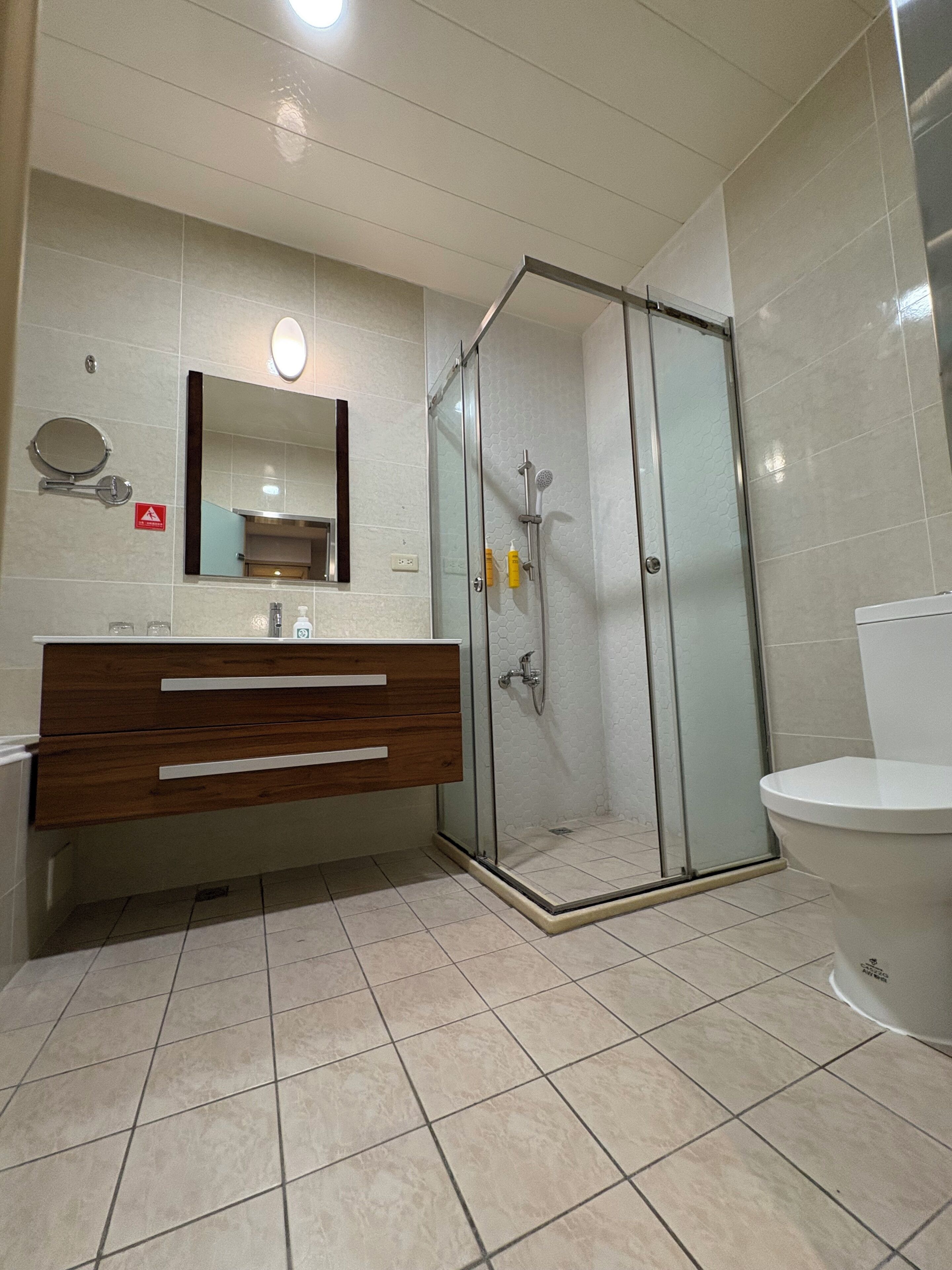 A bathroom with a glass-enclosed shower, a wooden vanity with a mirror, and a toilet.