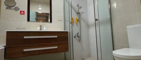 A bathroom with a glass-enclosed shower, a wooden vanity with a mirror, and a toilet.