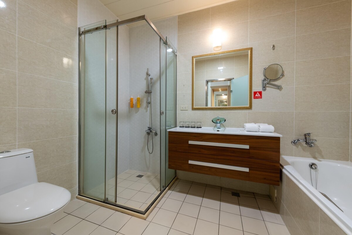 Un baño moderno con ducha envuelta en vidrio, tocador de madera, inodoro blanco y bañera.