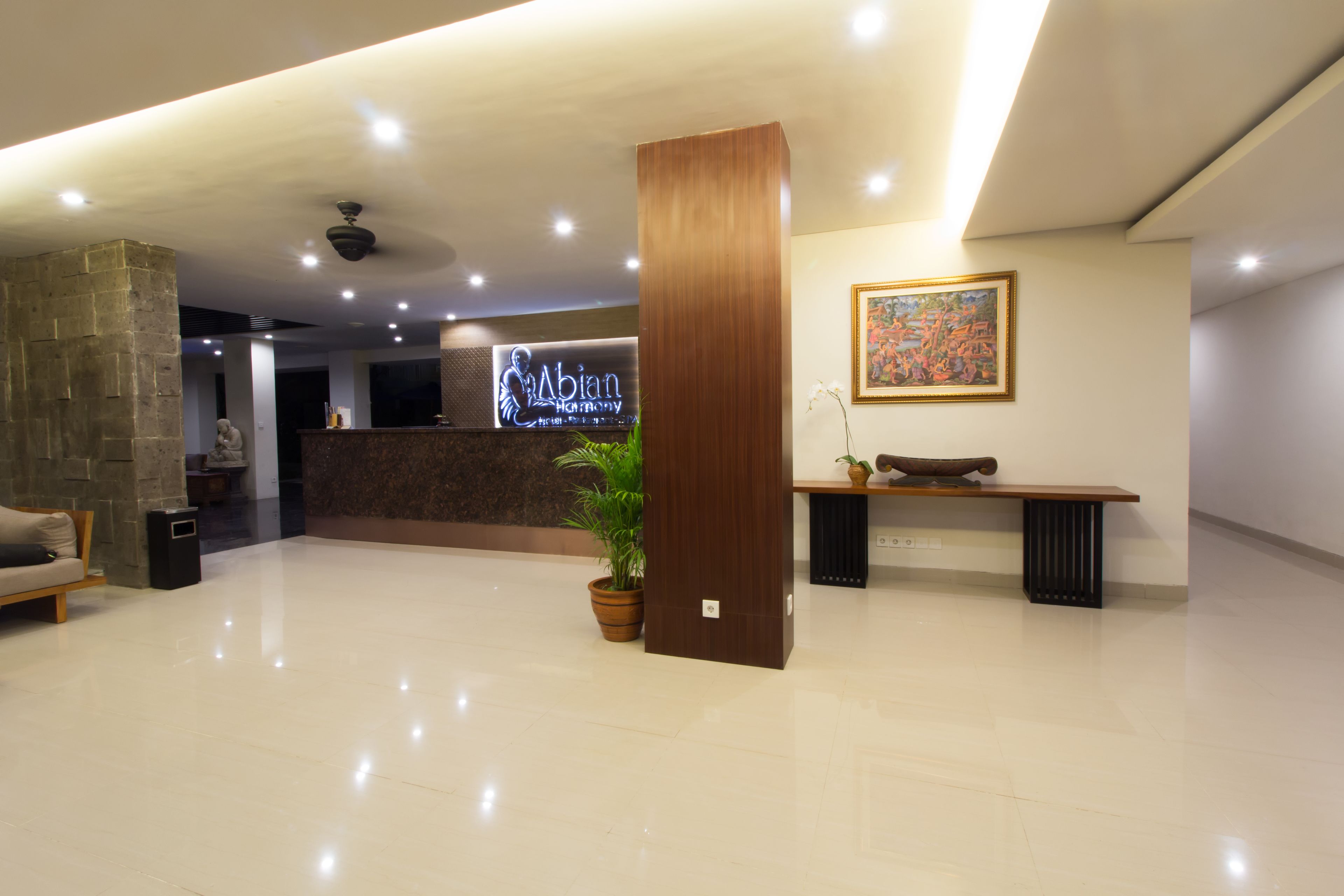 A hotel reception area with a reception desk, a potted plant, a bench, and a framed painting on the wall.
