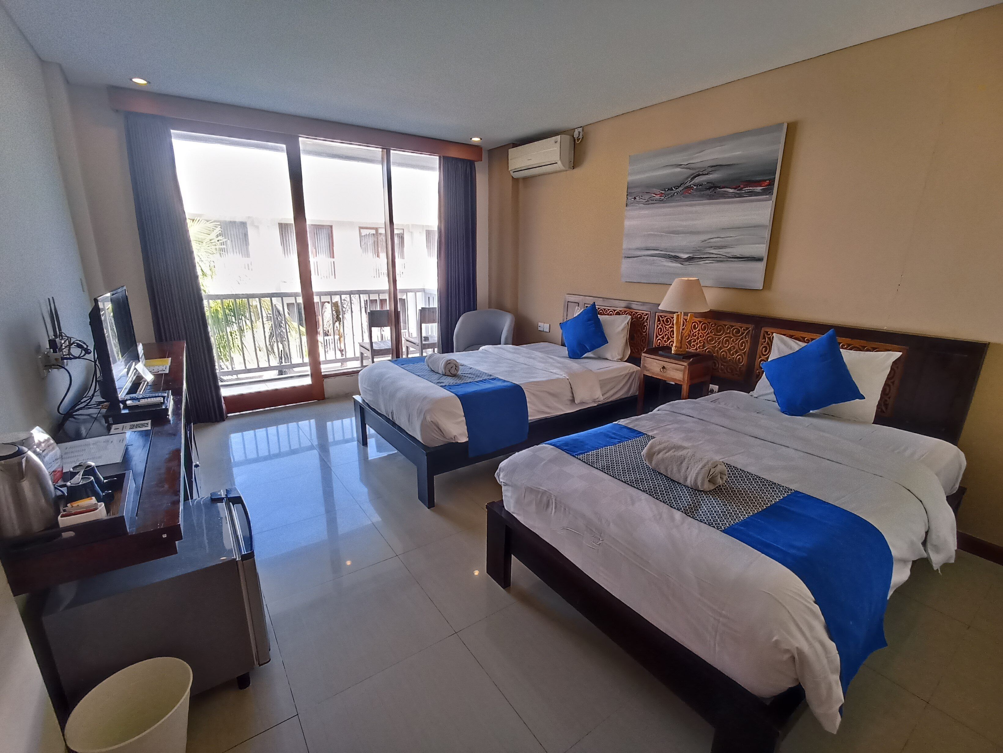 A hotel room with two beds, a desk, a chair, and a balcony with a view.