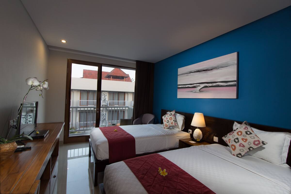 Ein Hotelzimmer mit zwei Betten, einem Schreibtisch, einem Sessel, einer Lampe und einem Bild an der Wand.
