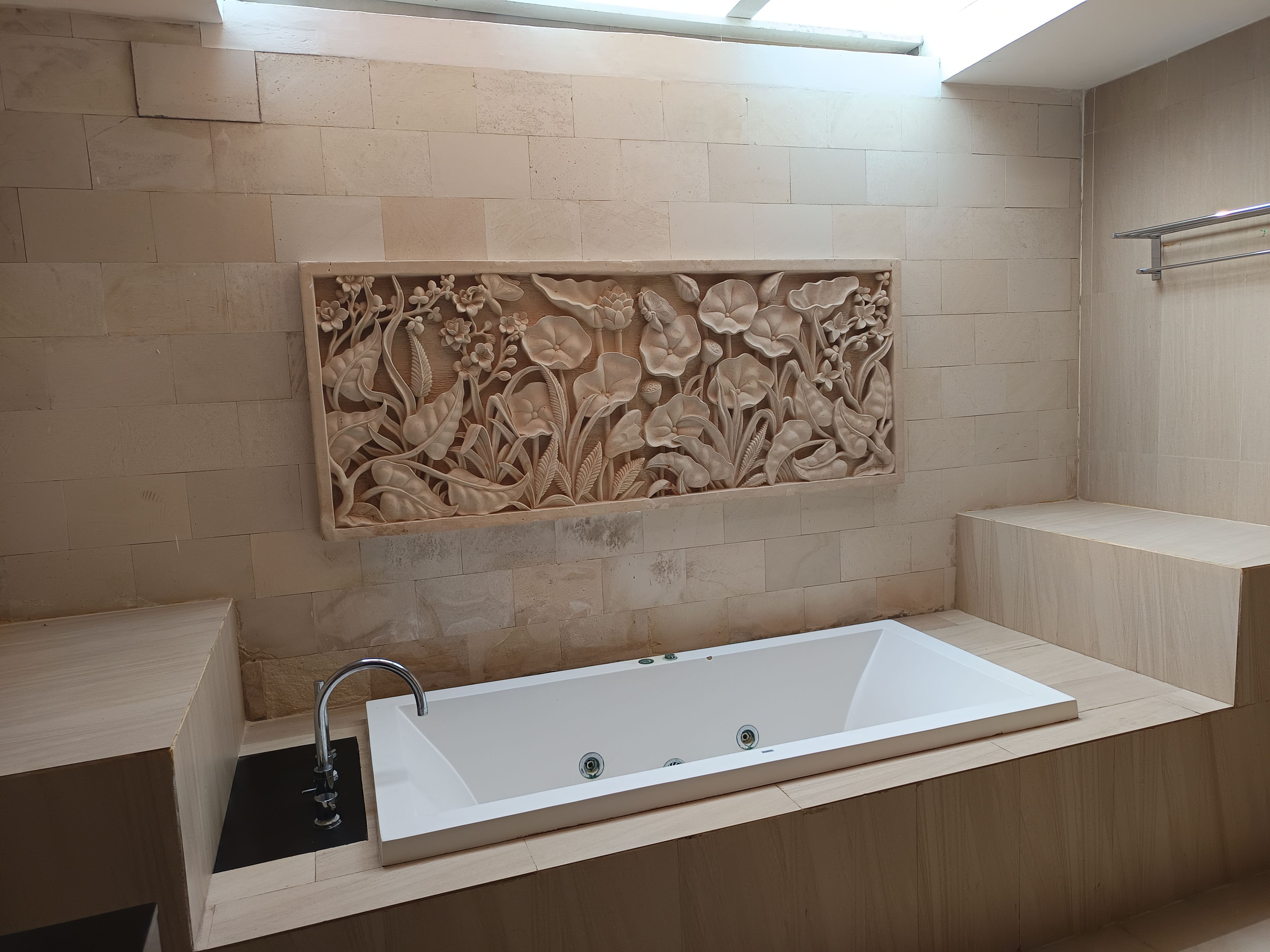 A bathroom with a freestanding bathtub, a wall-mounted sink, and a decorative floral panel.