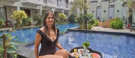 Una mujer sentada junto a una piscina con una bandeja de comida y bebidas.