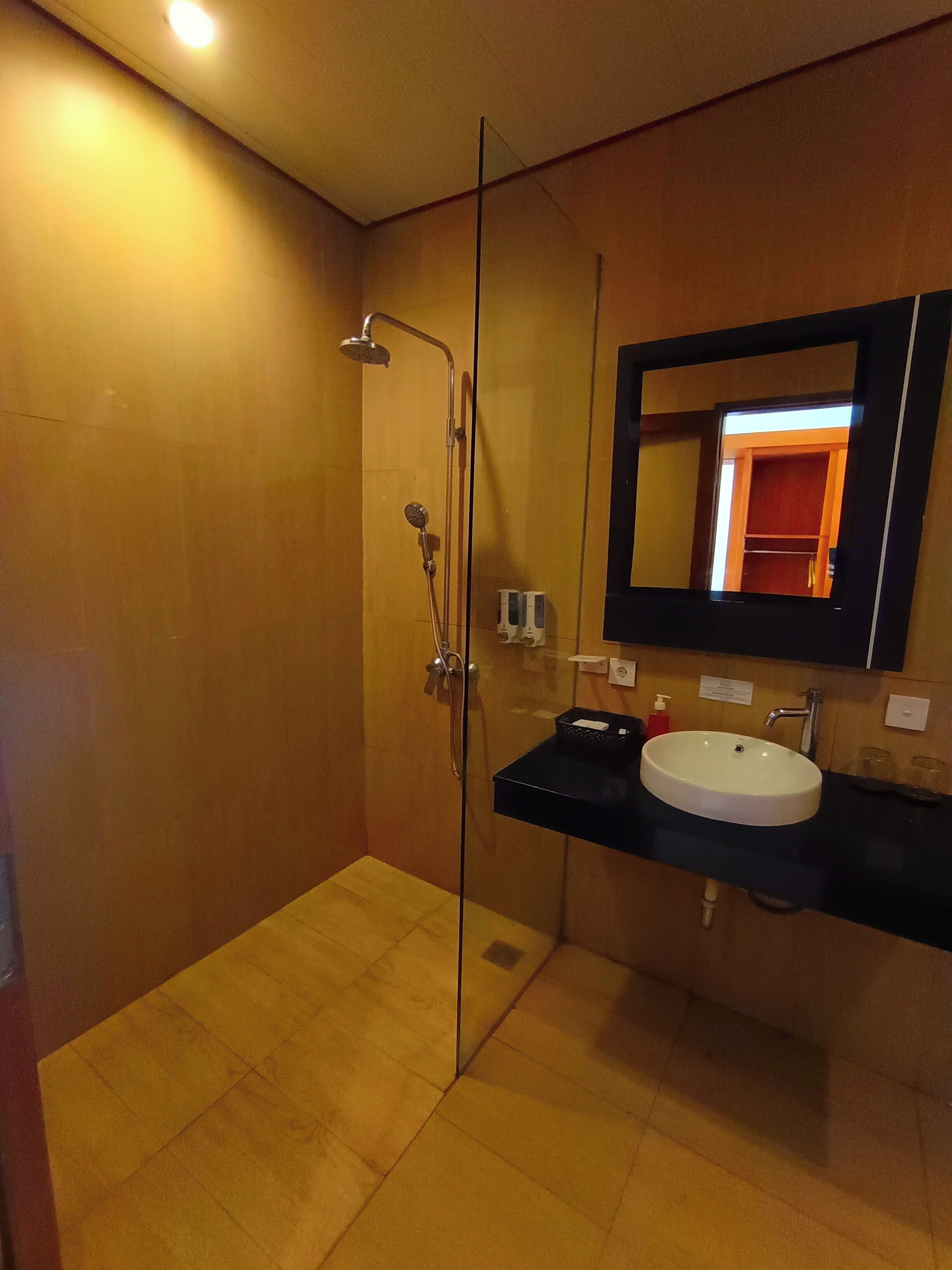 A modern bathroom with a glass-enclosed shower, a black countertop with a white sink, and a mirror above the sink.
