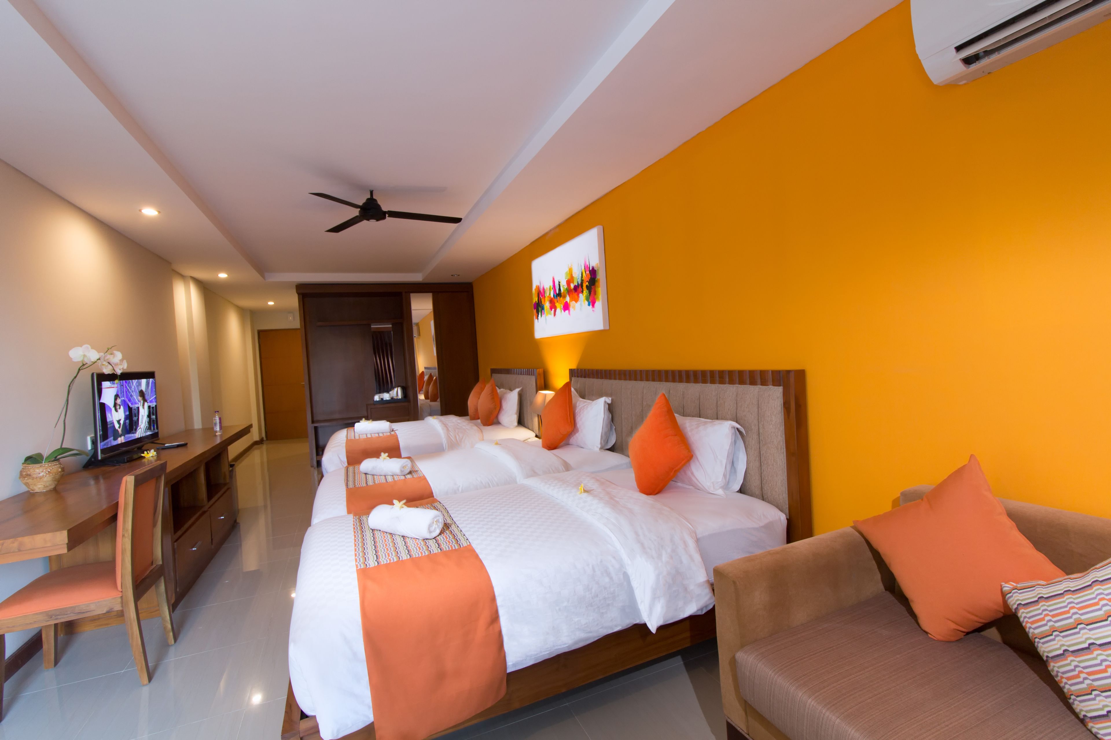 Une chambre d’hôtel avec un grand lit, un canapé, une télévision et un ventilateur de plafond.
