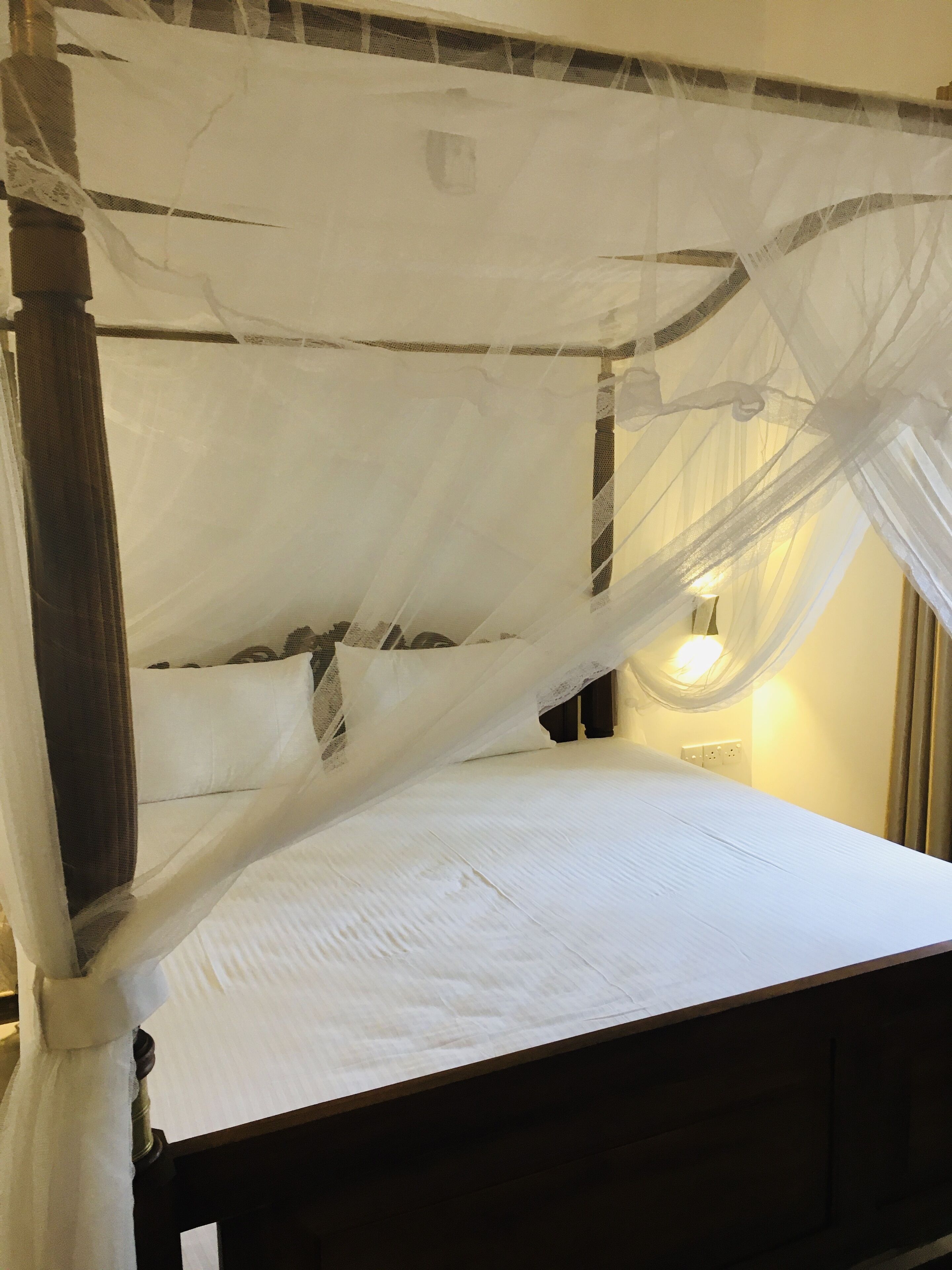 A bed with a canopy, a bedside table, and a wall-mounted light.