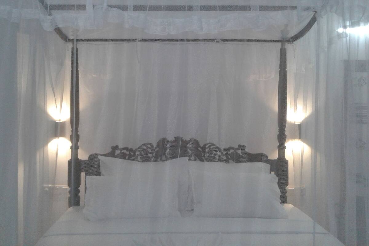 A four-poster canopy bed with white linens and two wall-mounted lamps.