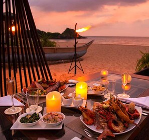 Una tavola imbandita per cena con piatti di pesce, una candela e vista sulla spiaggia al tramonto.