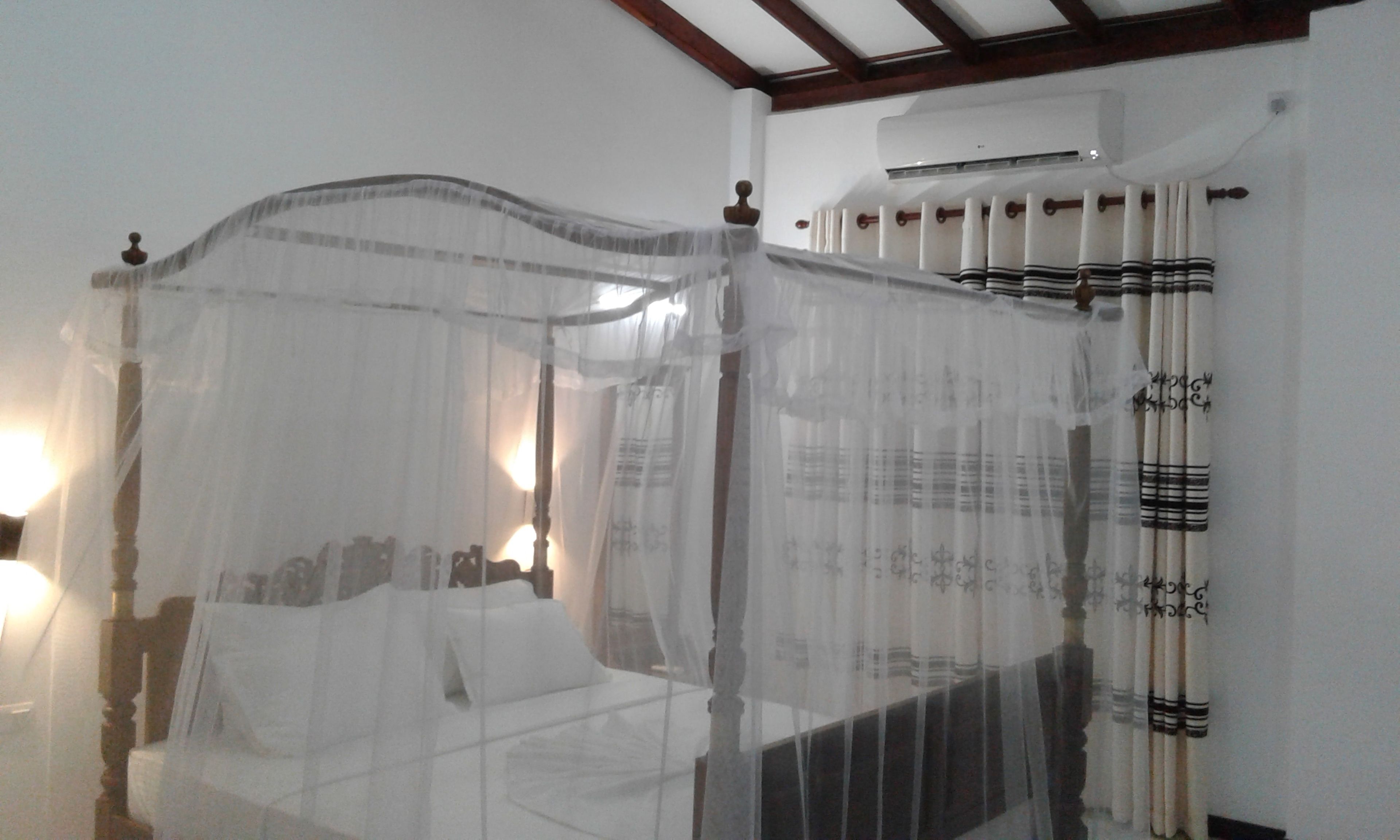 A four-poster bed with a canopy, a bedside table, and a wall-mounted air conditioning unit.