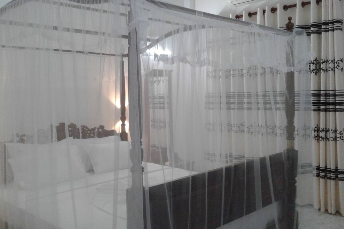 A bed with a canopy, curtains with a pattern, and a bed frame with a headboard.