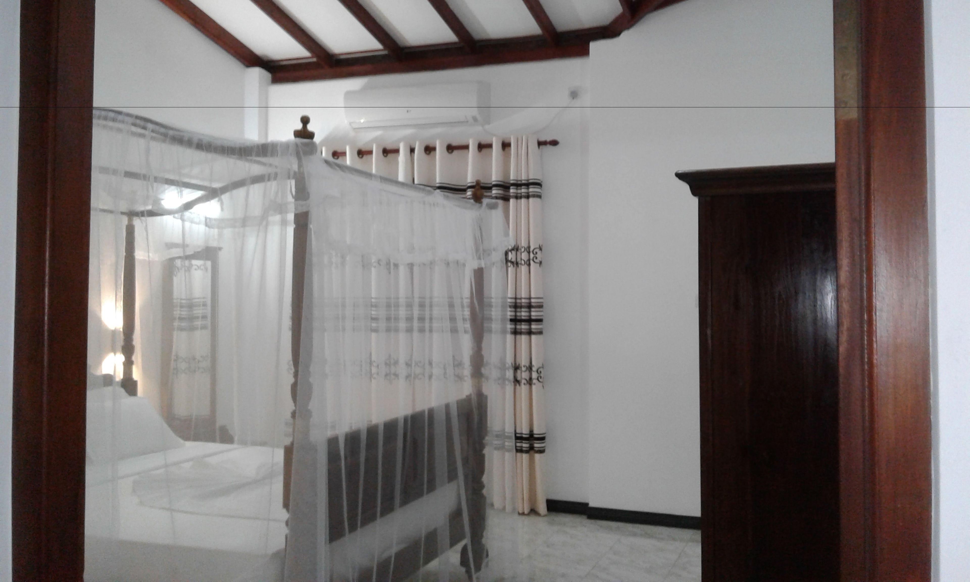 A bedroom with a bed, a wooden door, and a window with curtains.