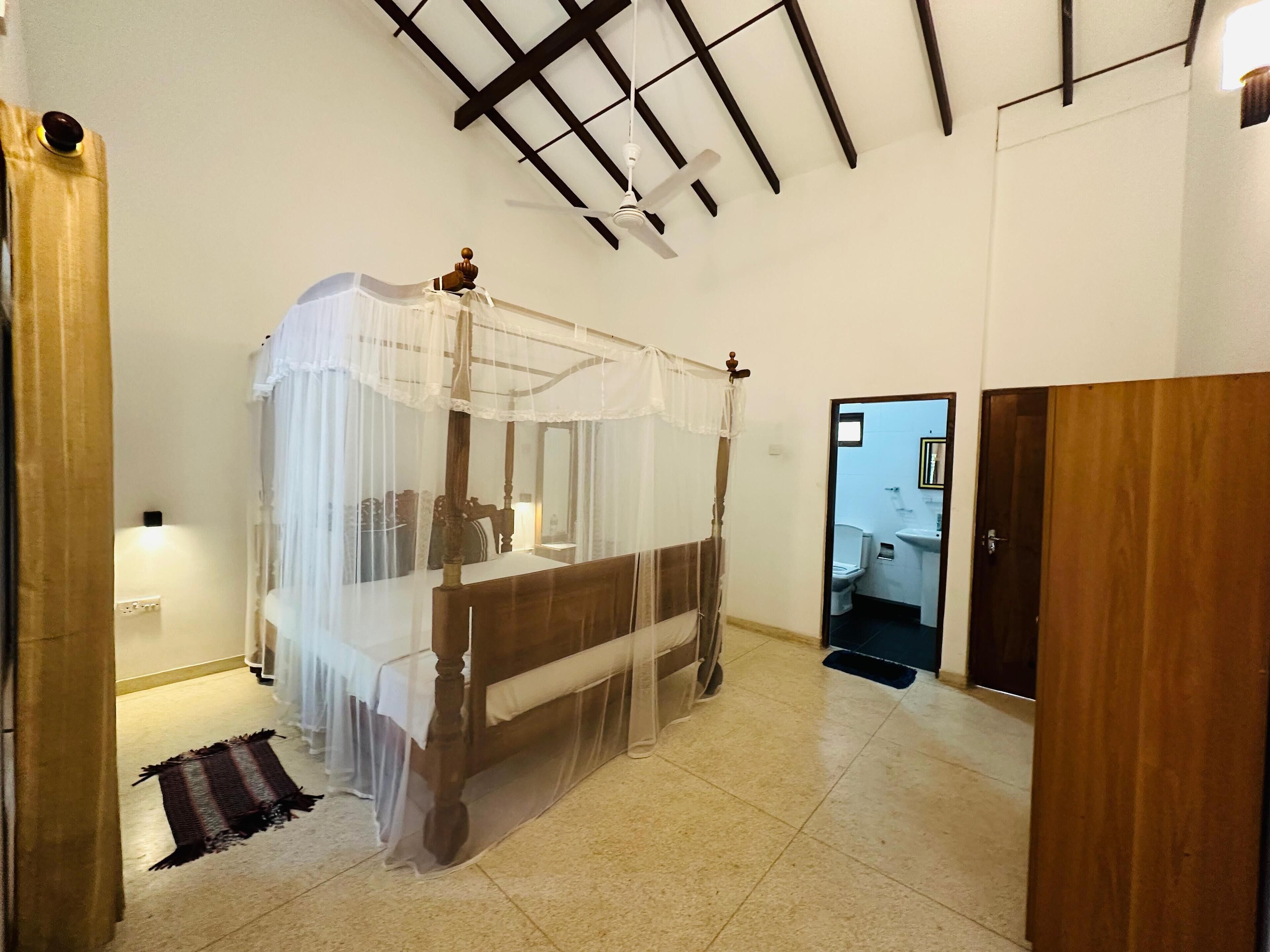 A four-poster bed with a canopy, a wooden wardrobe, and a bathroom visible through an open door.