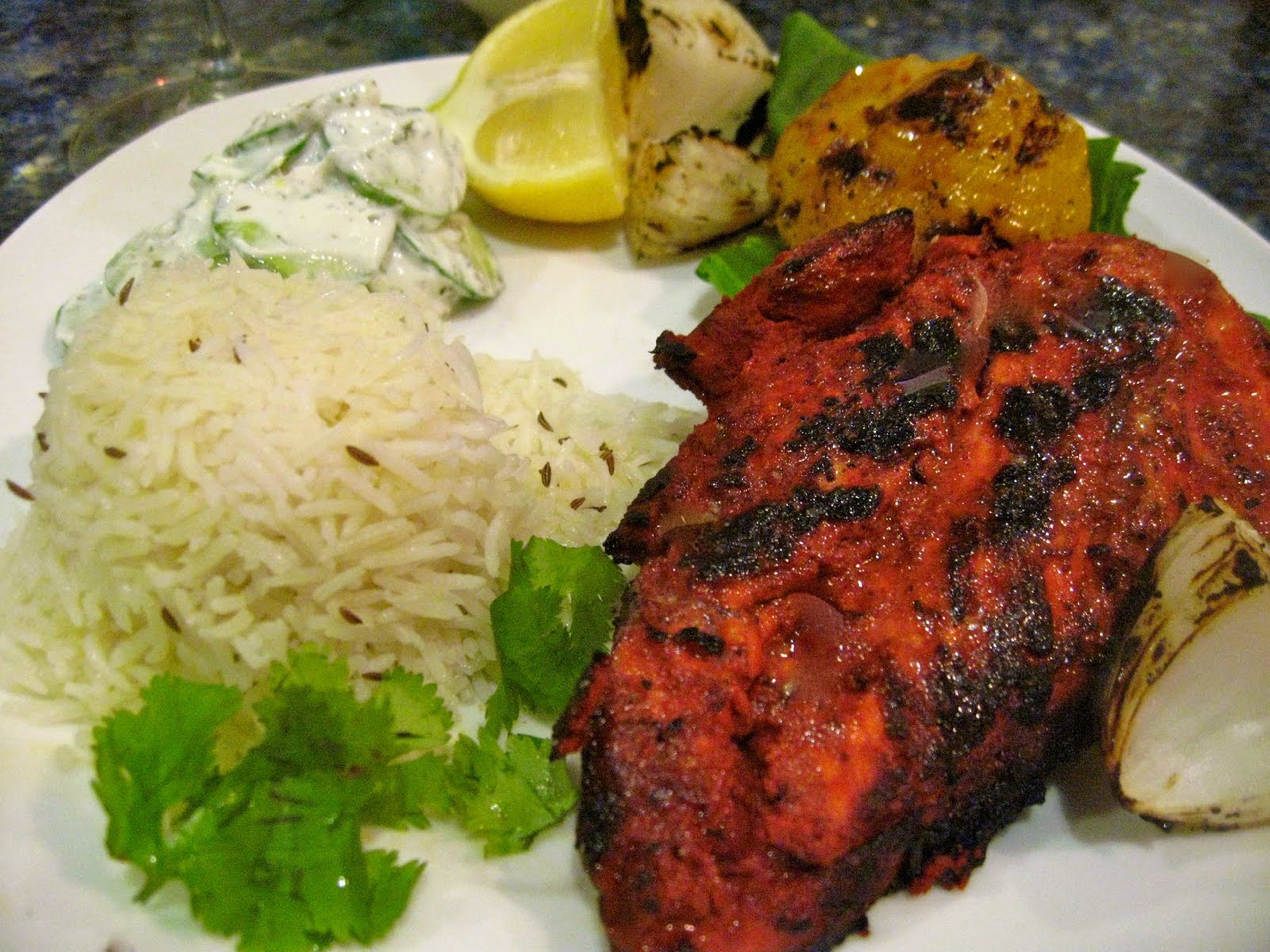 Une assiette comprenant de la viande grillée, du riz, des légumes grillés et un quartier de citron.