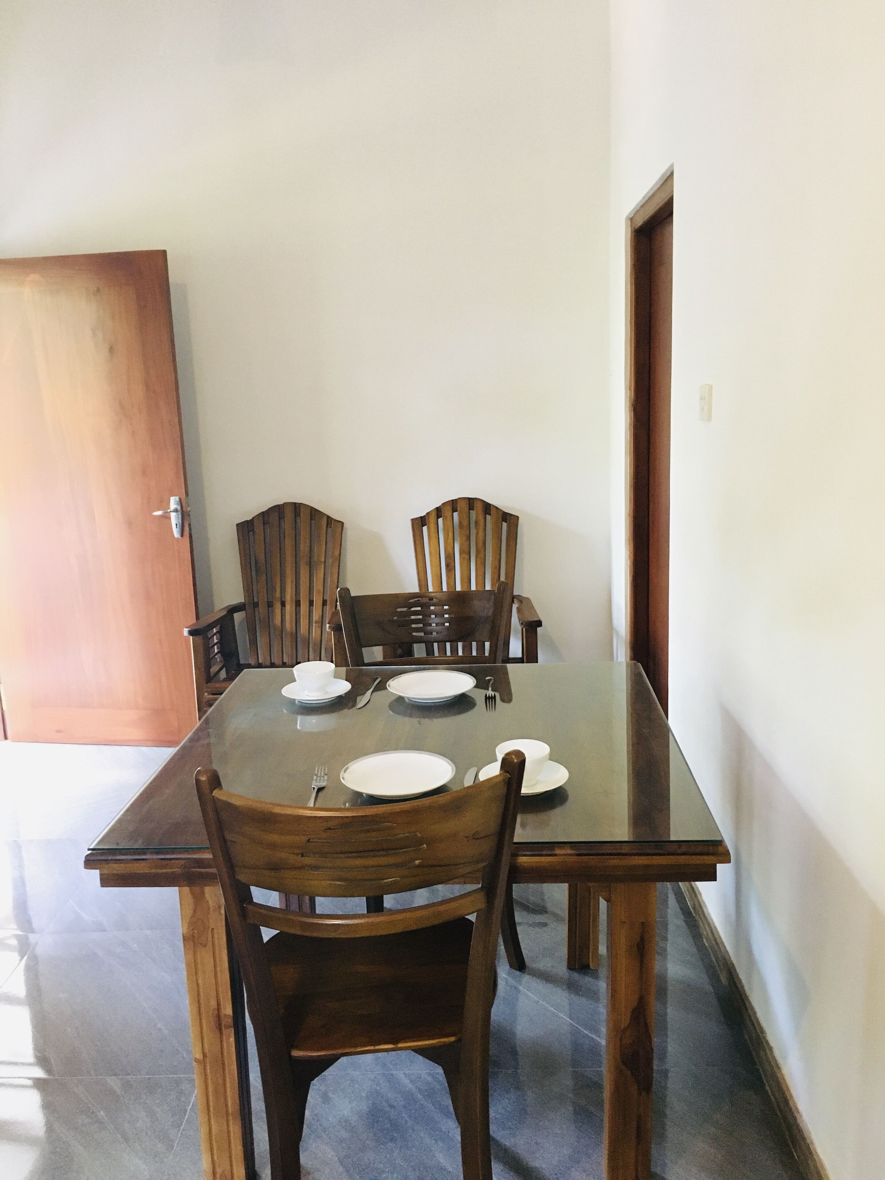 A dining area with a rectangular table set for four, surrounded by wooden chairs.