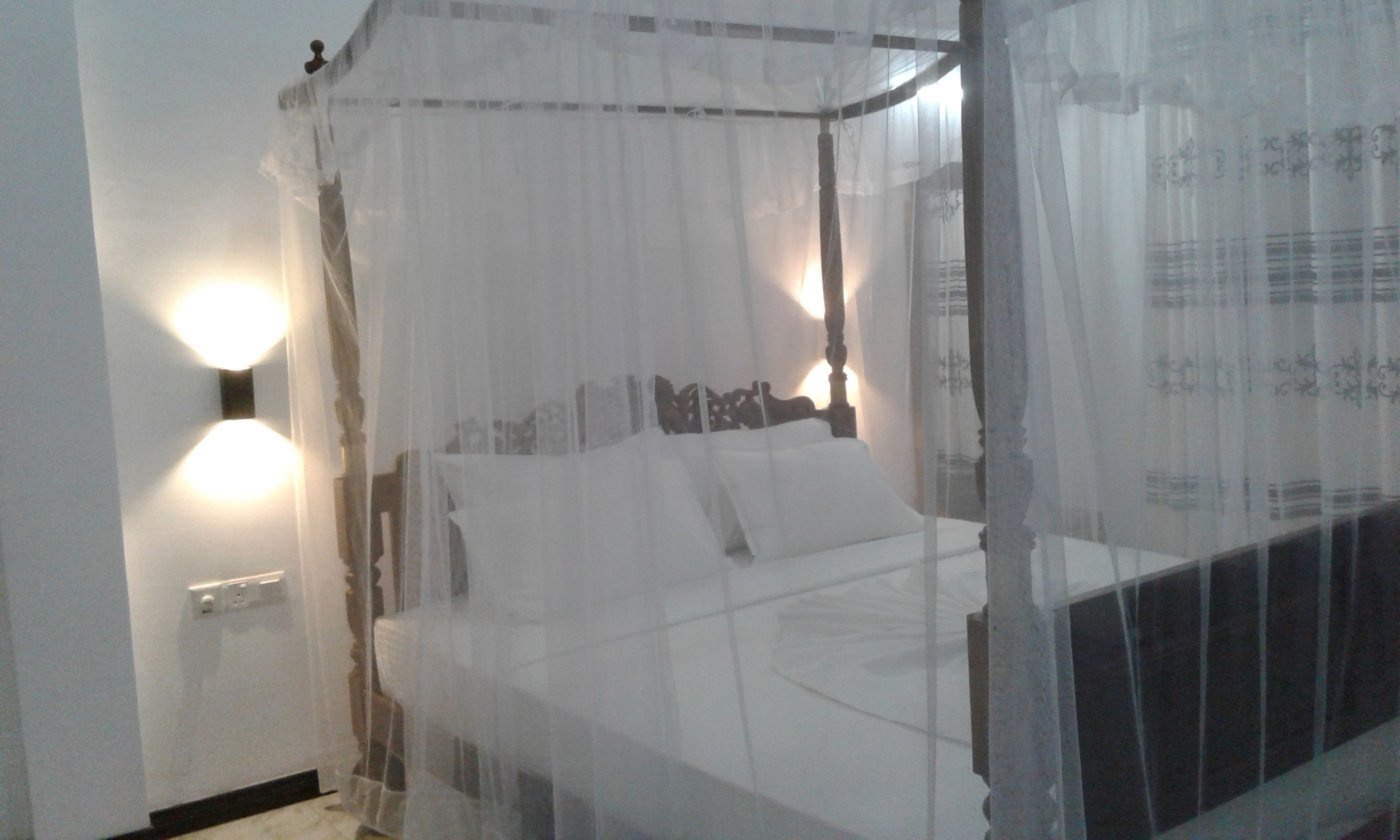A bed with a canopy, bedside lamps, and a wall socket.