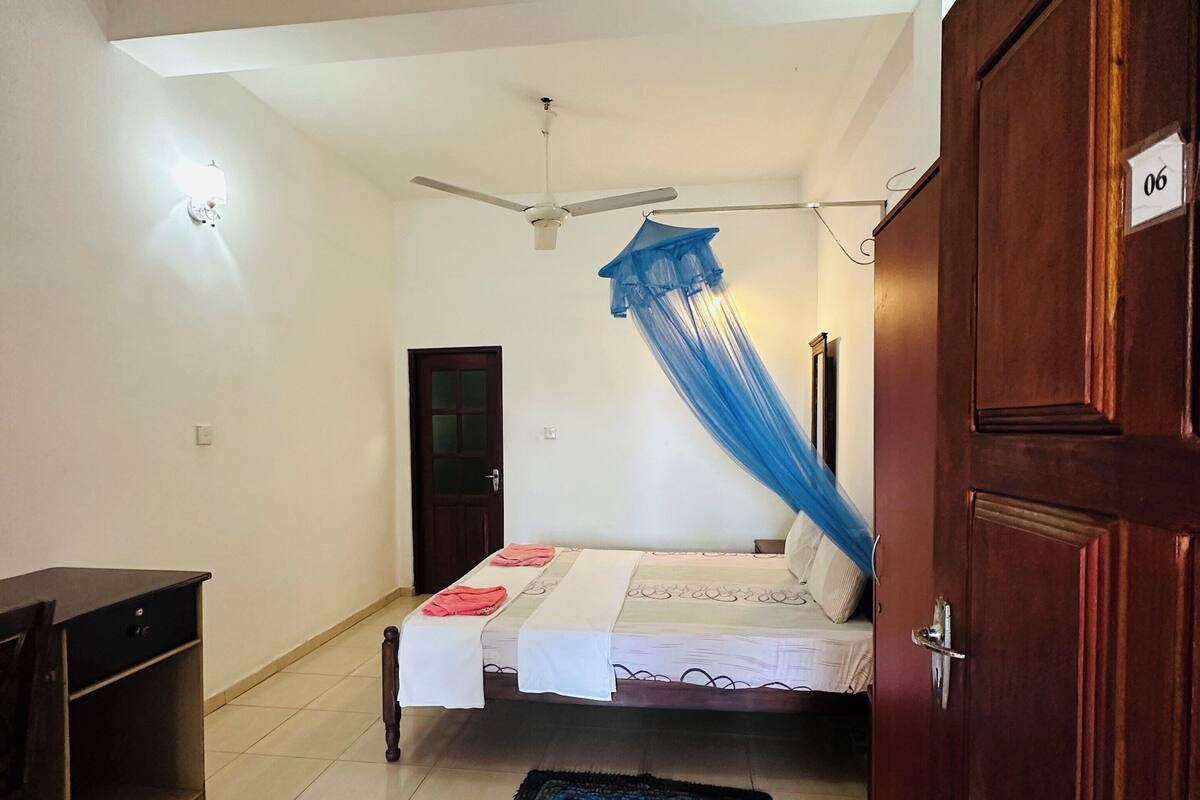 A bedroom with a bed, a ceiling fan, a nightstand, a wooden door, and a tiled floor.