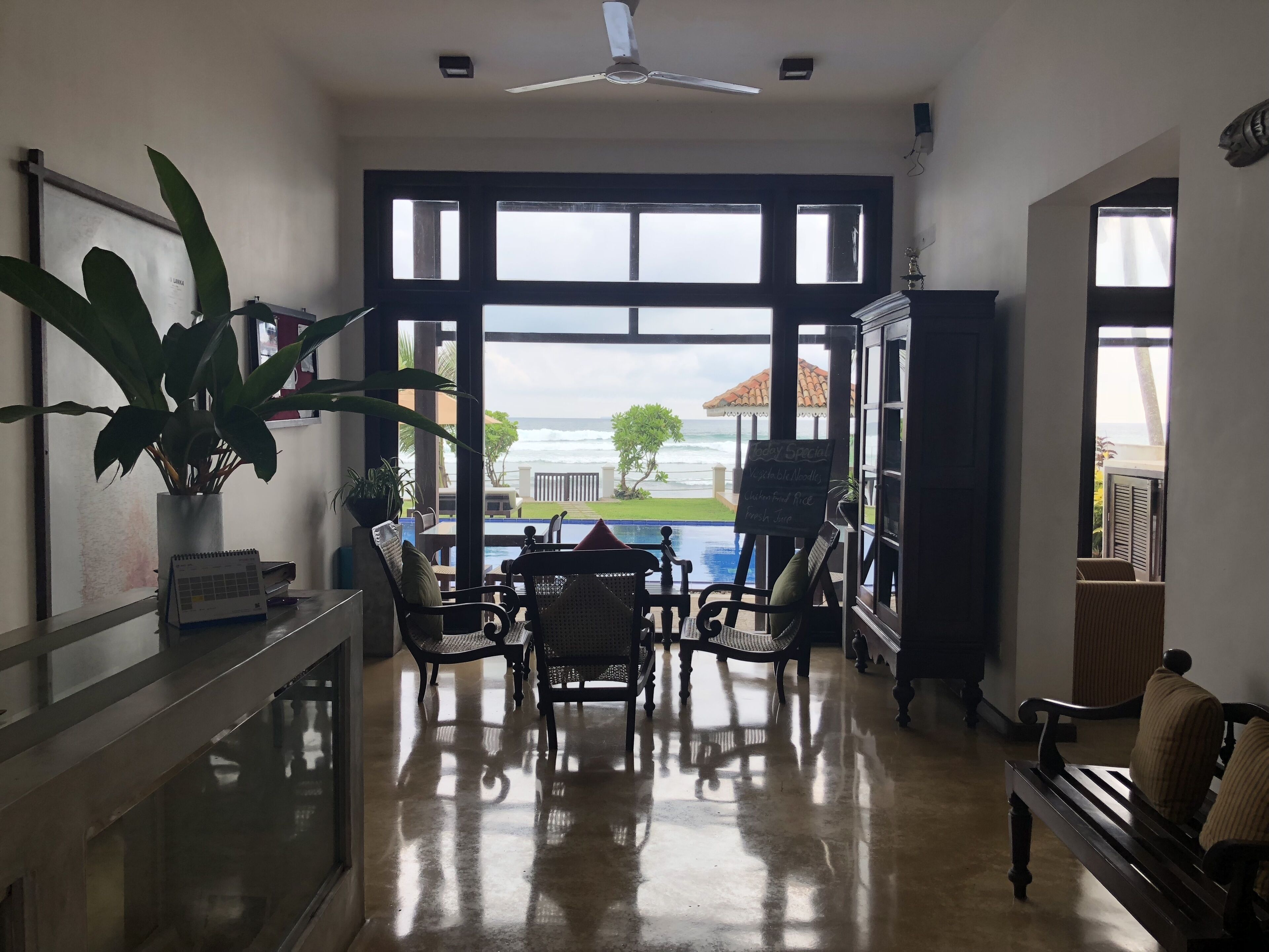 A spacious room with a large window overlooking the ocean, a ceiling fan, and a pool table.