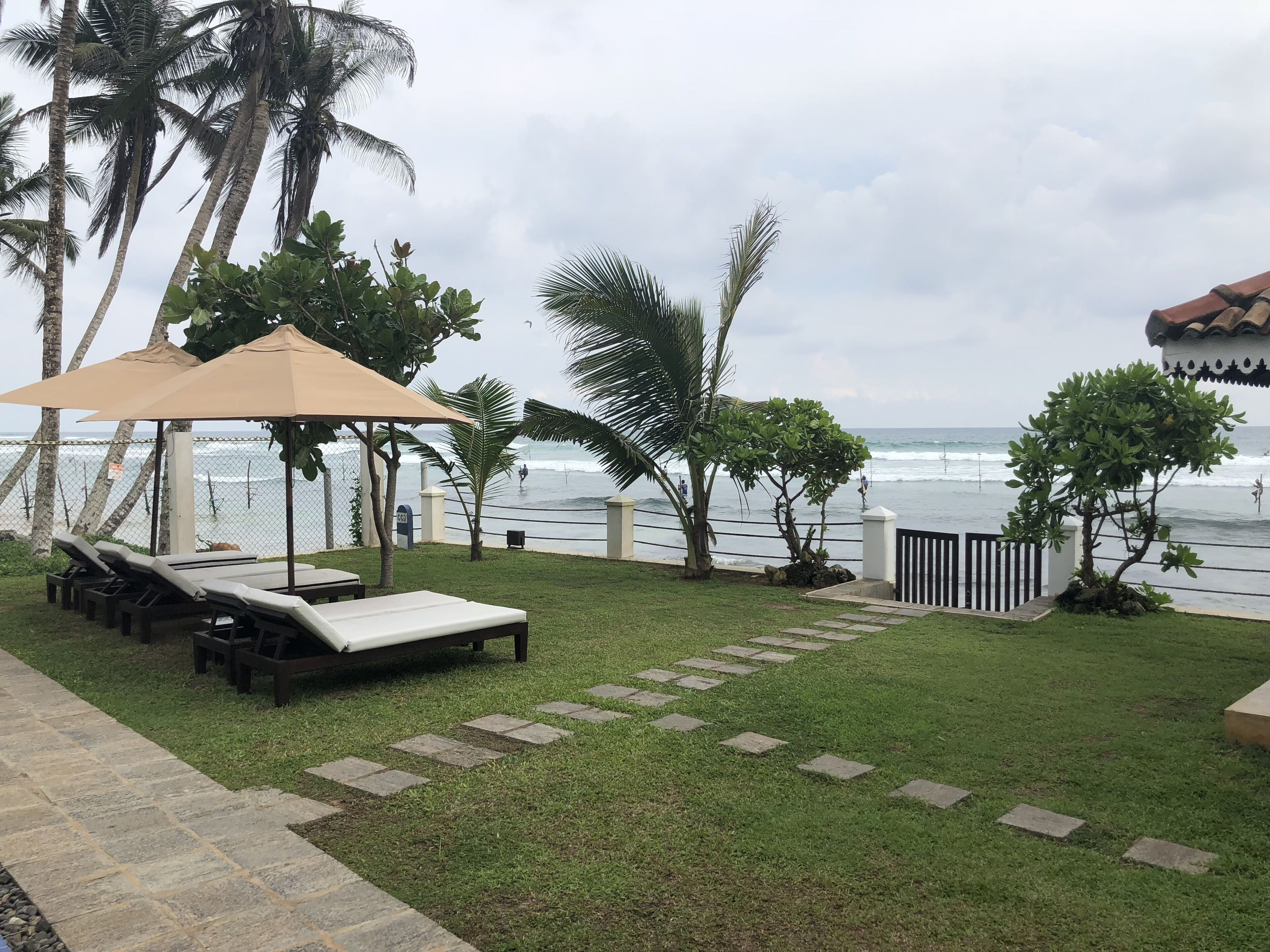 A beachside patio with lounge chairs and umbrellas, a stone pathway, and a view of the ocean.