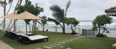 A beachside patio with lounge chairs and umbrellas, a stone pathway, and a view of the ocean.