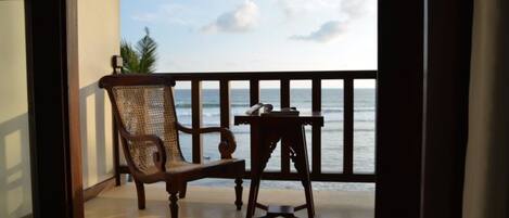 A wooden chair and a small table on a balcony with a view of the ocean.