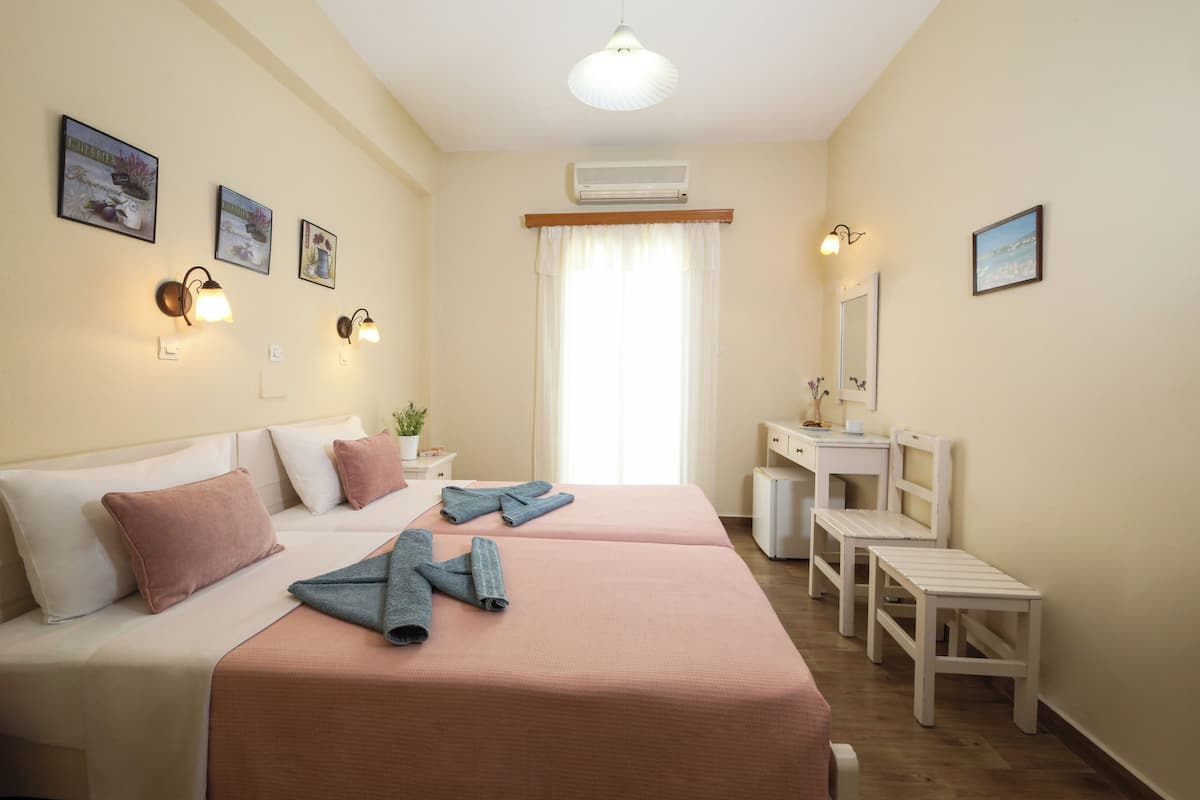 A hotel room with two beds, a desk, a chair, a mirror, and wall-mounted lights.