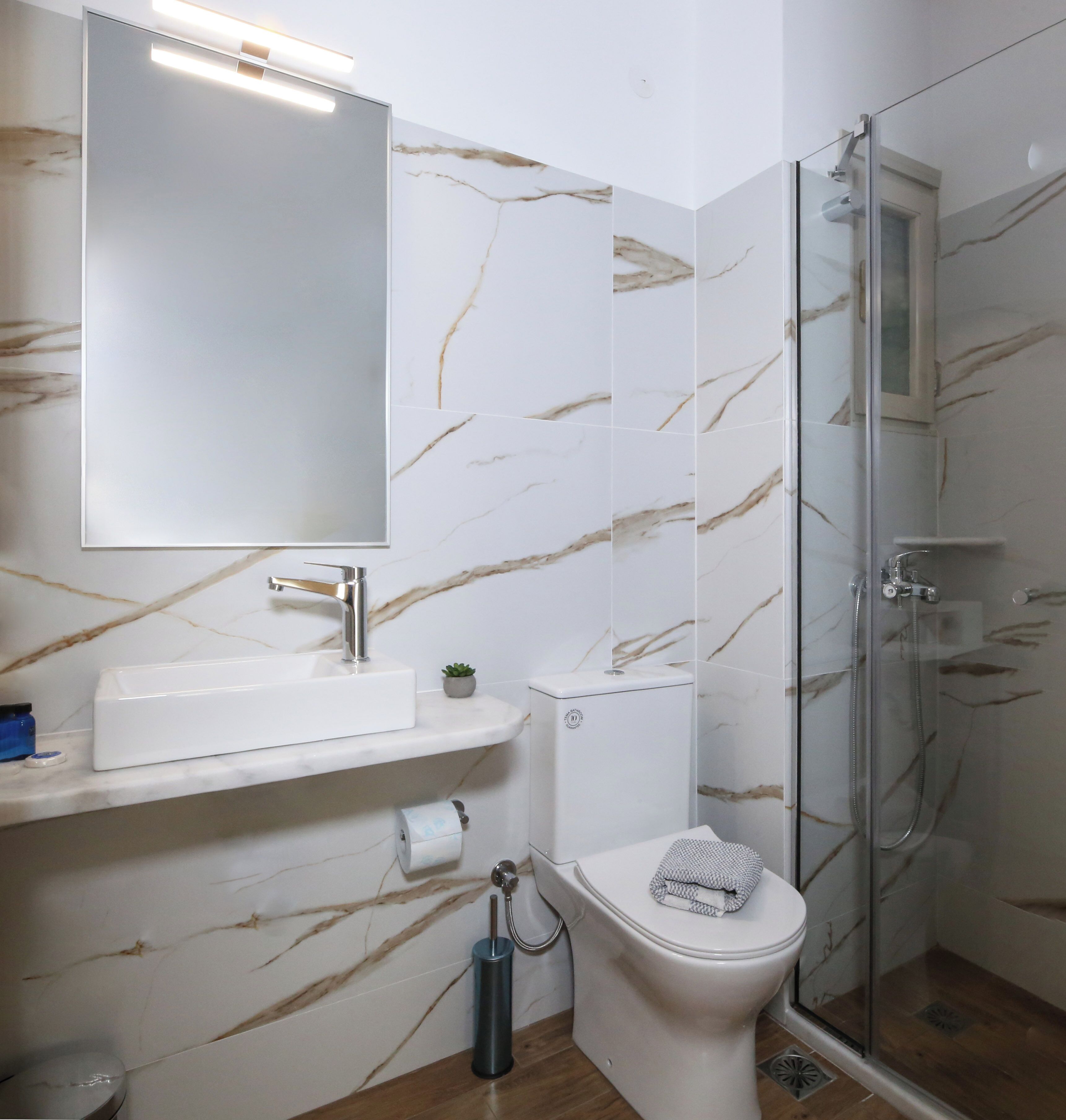 A bathroom with a marble-patterned wall, a white sink, a toilet, and a glass-enclosed shower.