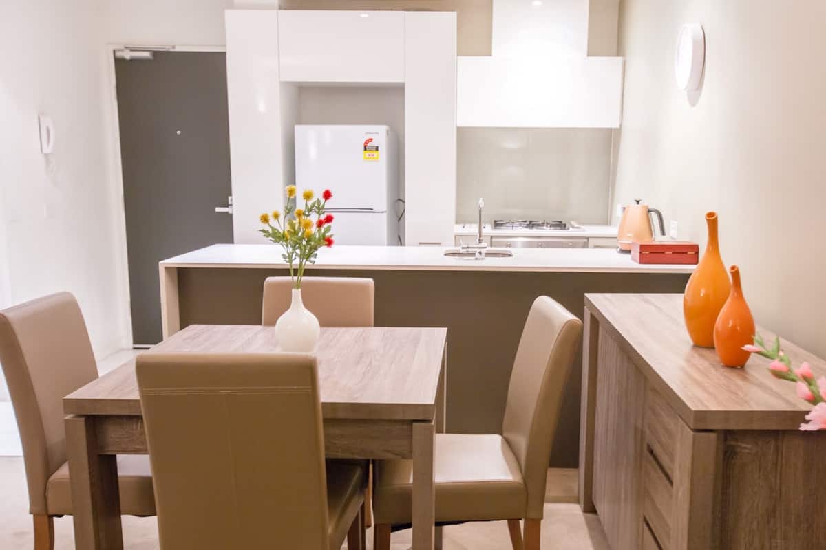 A modern kitchen with white cabinets, a built-in oven, and a dining area with a wooden table and chairs.